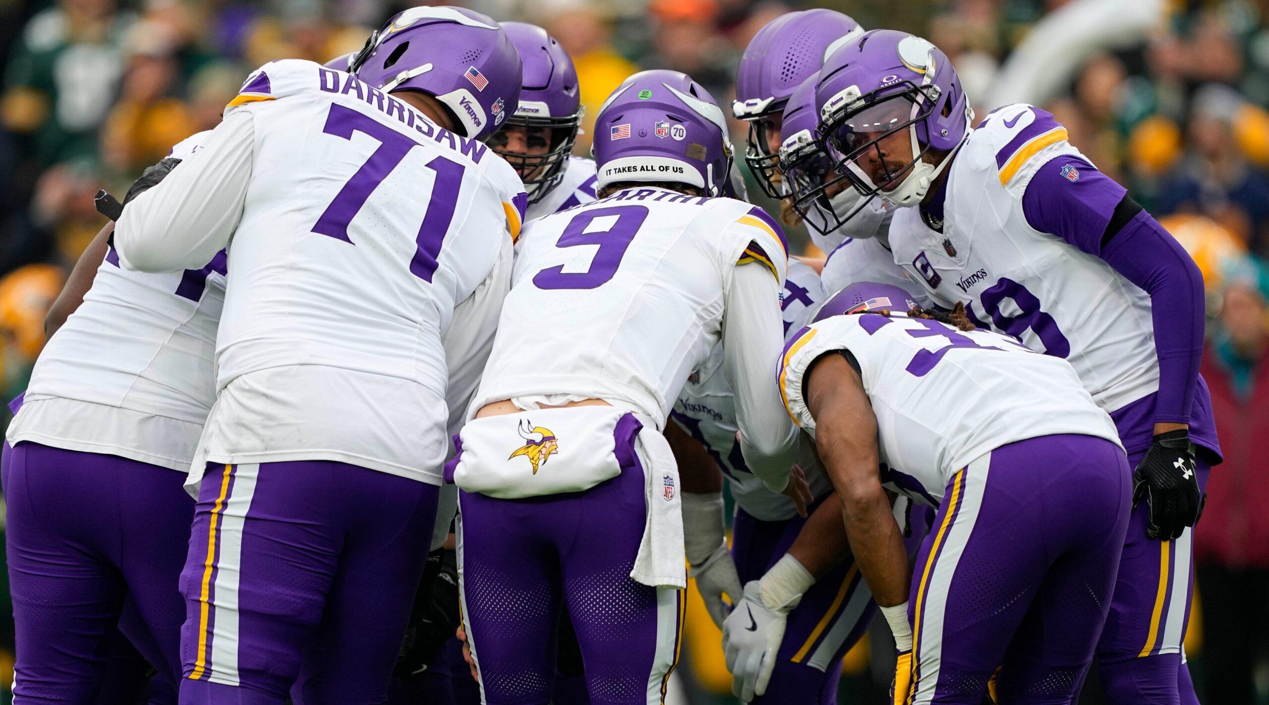 Minnesota Vikings players gather in the offensive huddle at Lambeau Field before a play against the Green Bay Packers with Christian Darrisaw visible on the left.