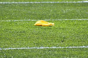 Yellow penalty flag lies on grass field with white yard line markings.