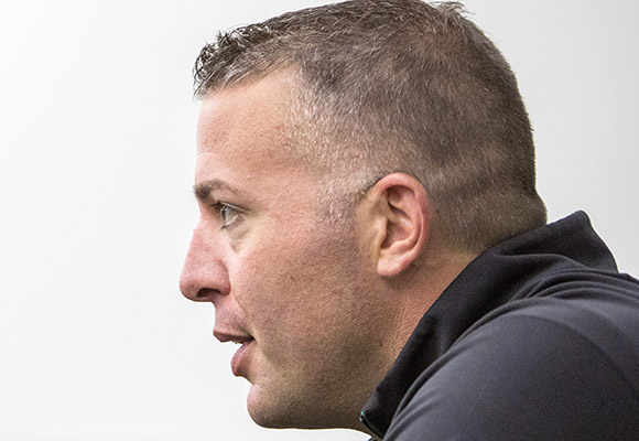 Man in dark hoodie shown in profile against white background.