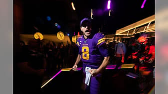Fan wearing purple number 8 Vikings jersey at night stadium event with crowd.