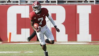Football player in maroon jersey running with ball on field.