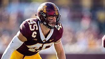 Football player in maroon and gold uniform crouched in ready position during game.