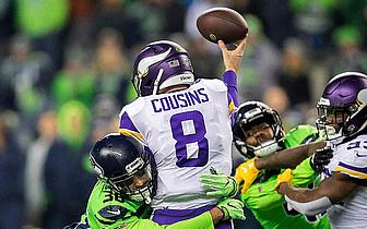 Vikings quarterback Cousins throws pass while defended by Seahawks players.