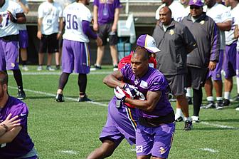 Vikings players in purple jerseys practice drill on grass field with coaches.
