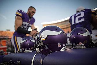 Vikings players in purple uniforms with helmets on sideline during game.