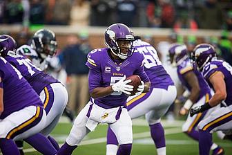 Minnesota Vikings player holds football during offensive play at home stadium.