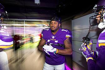 Player in purple Vikings jersey prepares in locker room before game.