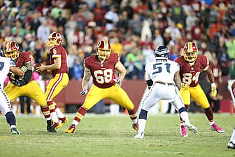 Washington football players in burgundy and gold jerseys engage during game action.