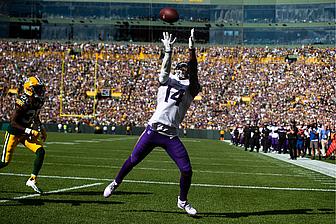 Vikings receiver jumps for catch in stadium with yellow seats.