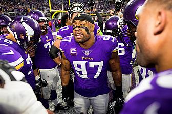 Vikings players in purple jerseys gather on sideline during game.
