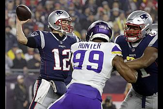 Patriots quarterback throws football while Vikings defender Hunter closes in during game.