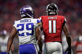 Two NFL players standing side by side during game, one wearing purple Vikings jersey number 29