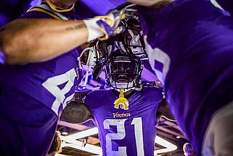 Vikings player in purple #21 jersey holds helmet above head in celebration.