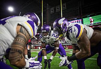 Vikings players in purple jerseys huddle together on field at night.