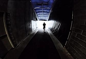 Runner jogging through dark tunnel toward bright light ahead.