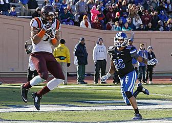 Football player in maroon jersey catches ball while defender in blue pursues.