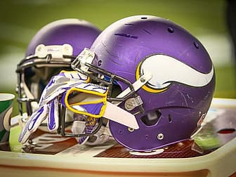 Two purple Vikings helmets with white 'V' logo displayed on field surface.