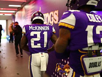 Player wearing purple Vikings jersey number 21 McKinnon in locker room.