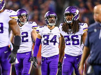Minnesota Vikings players in white jerseys stand together during game.
