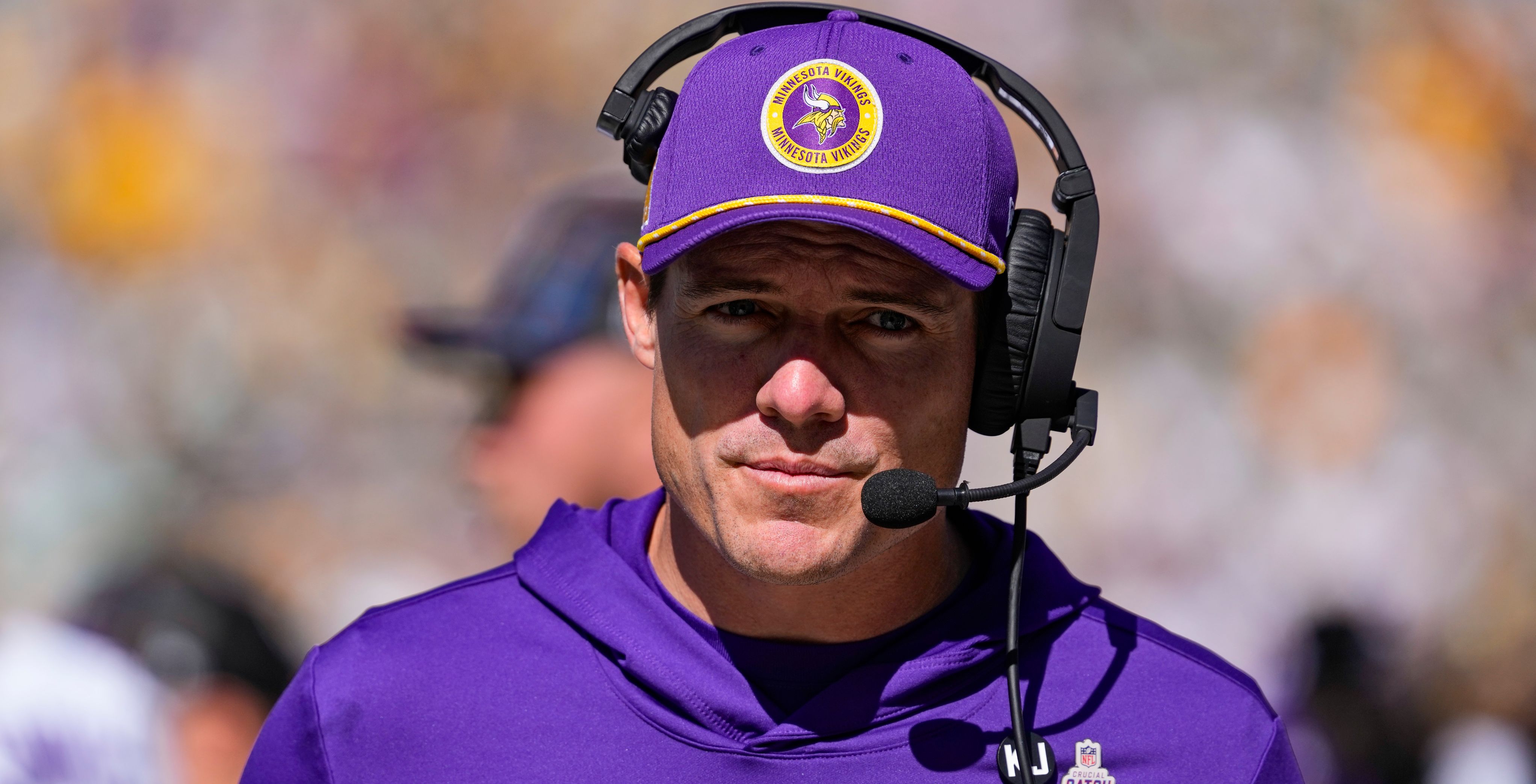 Coach wearing purple Vikings visor and headset on sideline.