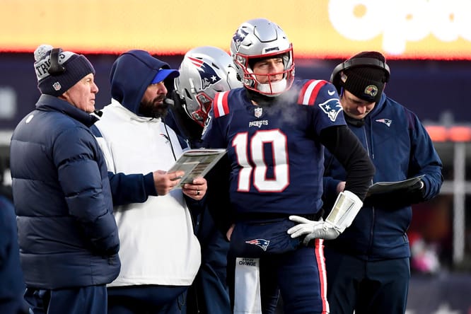 Patriots quarterback Mac Jones talks with coaches on the sideline.