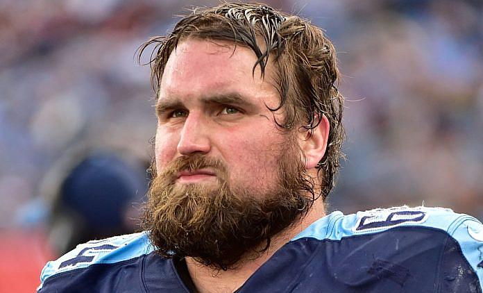 Bearded football player in dark blue jersey on sideline.