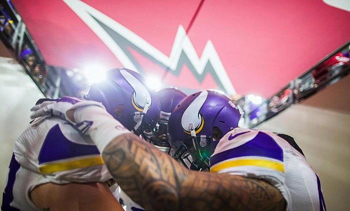Minnesota Vikings players huddle together wearing purple jerseys with helmets.