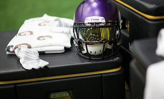 Purple football helmet with white gloves on black bench with gold trim.