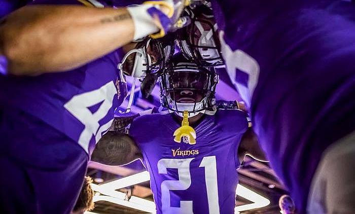 Vikings player in purple #21 jersey holds helmet above head in celebration.