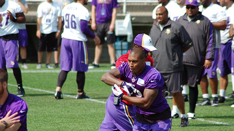 Vikings players in purple jerseys practice drill on grass field with coaches.