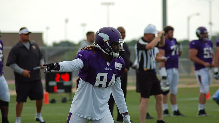 Vikings player in purple jersey pointing during practice drill on field.