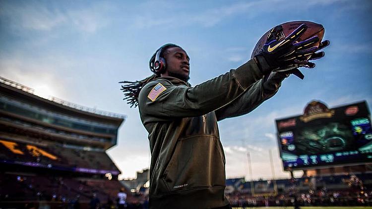 Player in Vikings gear holding football helmet at stadium during daytime.