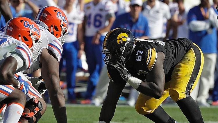 Football player in black and gold jersey in defensive stance during game.
