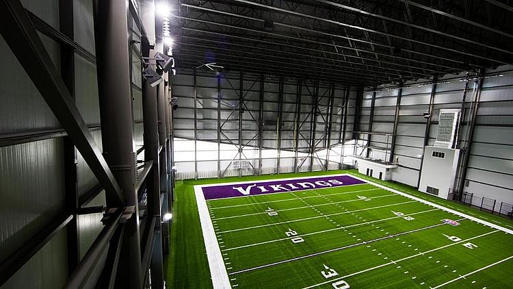 Indoor football field with purple Vikings logo on green turf.