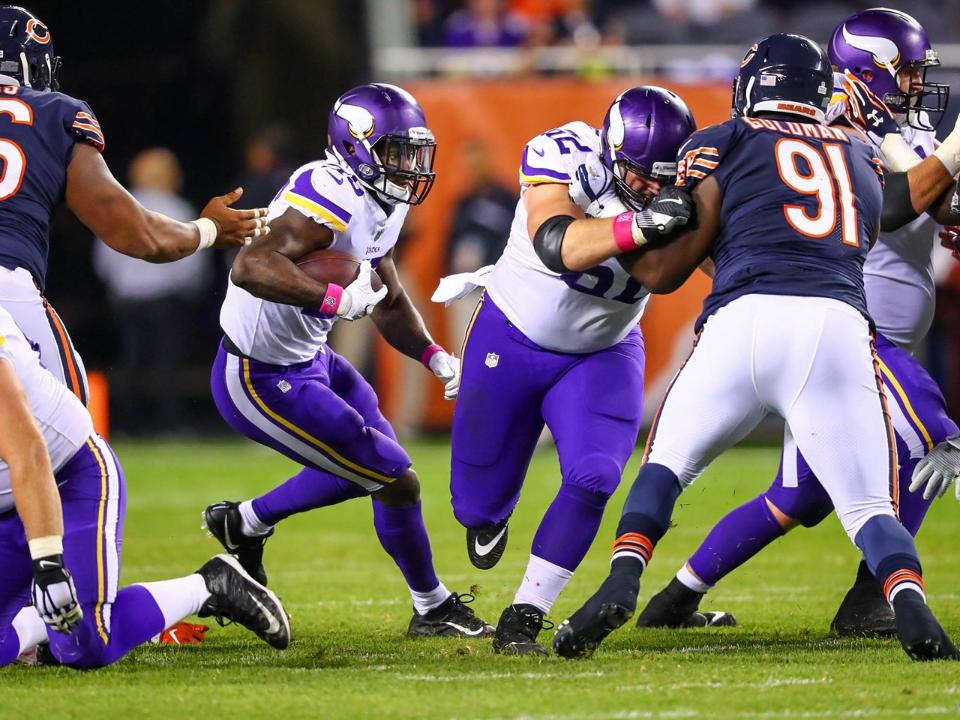 Minnesota Vikings player runs with football during night game against opposing team.