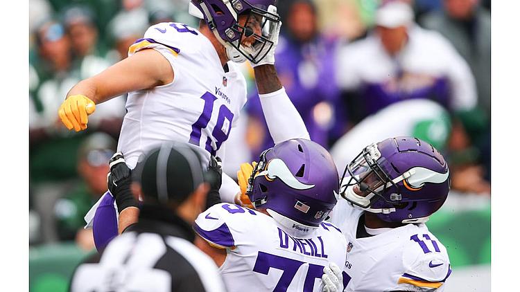 Minnesota Vikings player leaps and celebrates with teammates during NFL game.