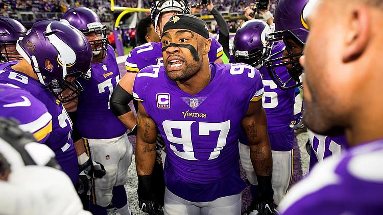 Vikings players in purple jerseys gather on sideline during game.