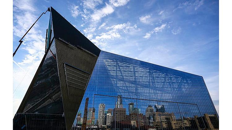 Modern glass building with city skyline reflection against blue sky.