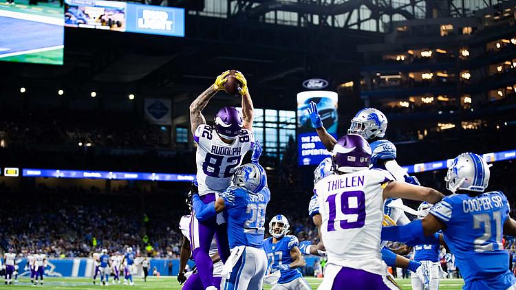 Vikings player jumps to catch football during NFL game in stadium.