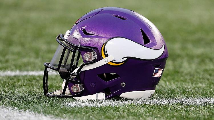 Purple Minnesota Vikings football helmet on grass field with yard line.