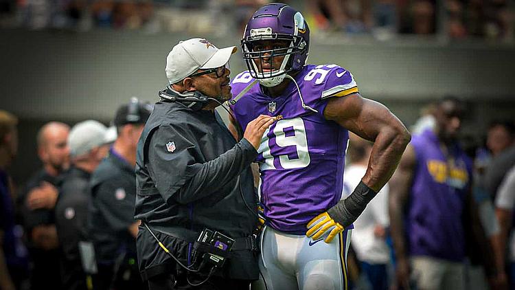 Coach speaks with Vikings player wearing purple jersey number 19.