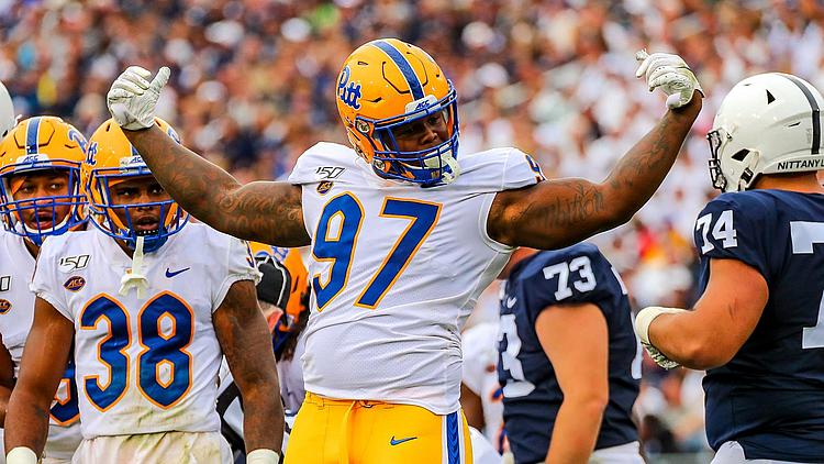 Football player #97 celebrates with arms raised during game with crowd behind.
