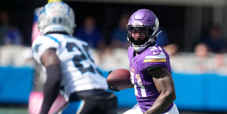 Cam Akers runs after a catch for the Vikings while defended by Xavier Woods against the Panthers in 2023.