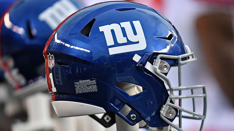 Blue NFL helmet with "ny" logo on blurred sideline background.