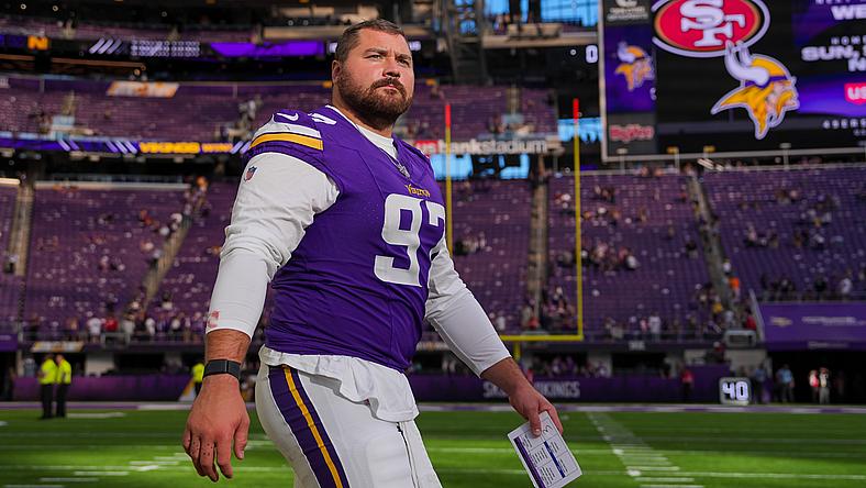 Minnesota Vikings player in purple jersey stands on field at stadium.