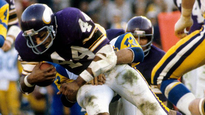 Vikings player in purple jersey carries football during game action.