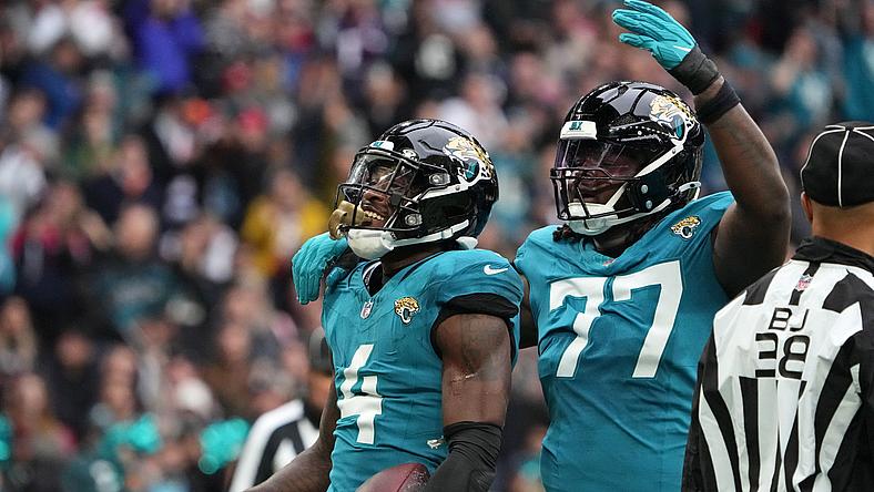 Two football players in teal jerseys celebrate during game with crowd behind.
