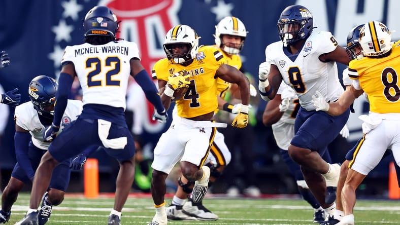 Wyoming running back Harrison Waylee rushing while a Toledo defender attempts a tackle in the Arizona Bowl. Vikings draft scenarios.